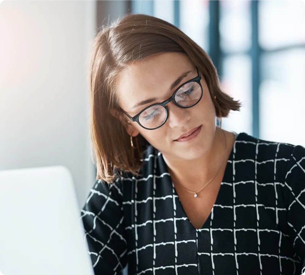 Woman with glasses working on a laptop in a bright office