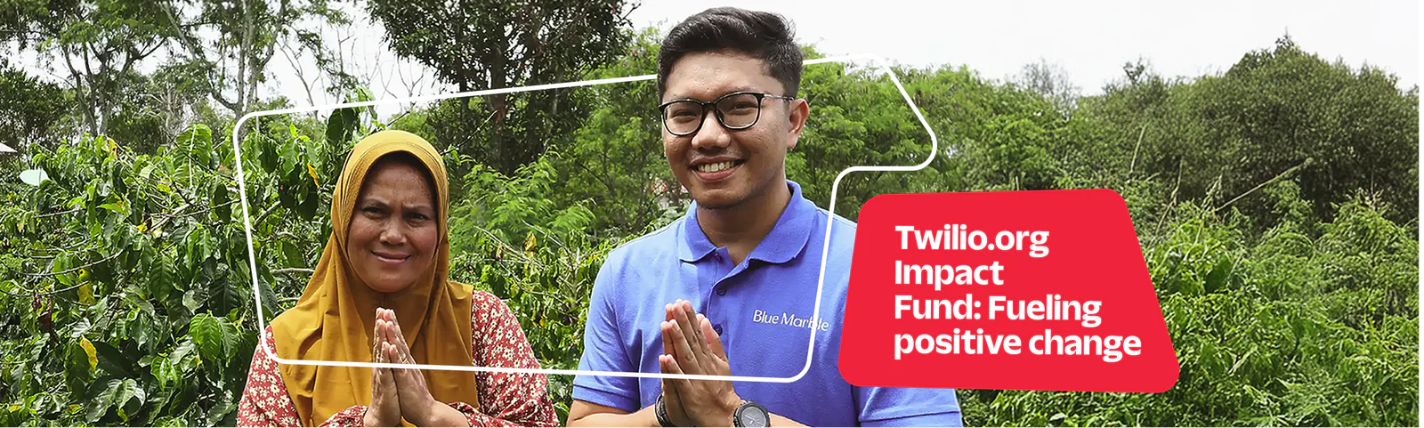 Two smiling individuals standing outdoors with trees in the background, hands together in a greeting. Two smiling individuals standing outdoors with trees in the background, hands together in a greeting.