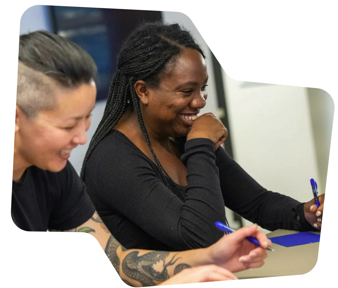 Two colleagues smiling and writing notes during a workshop Two colleagues smiling and writing notes during a workshop.